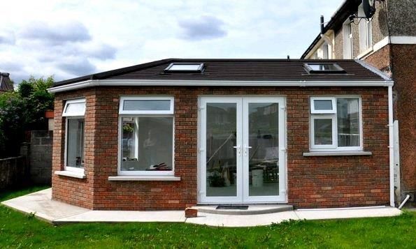 Brick-walled extension with white-framed windows, a double door, and a dark roof on a grassy lawn.