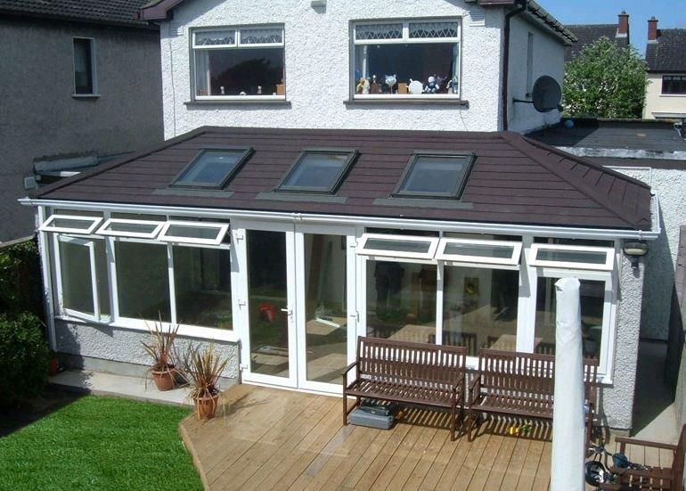 A brown-roofed sunroom with three skylights and a deck in a grassy backyard.