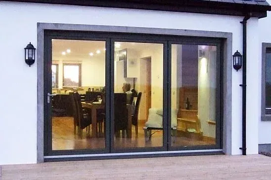 Large glass folding doors on white house, interior with furniture visible. Exterior has lamps, a deck.
