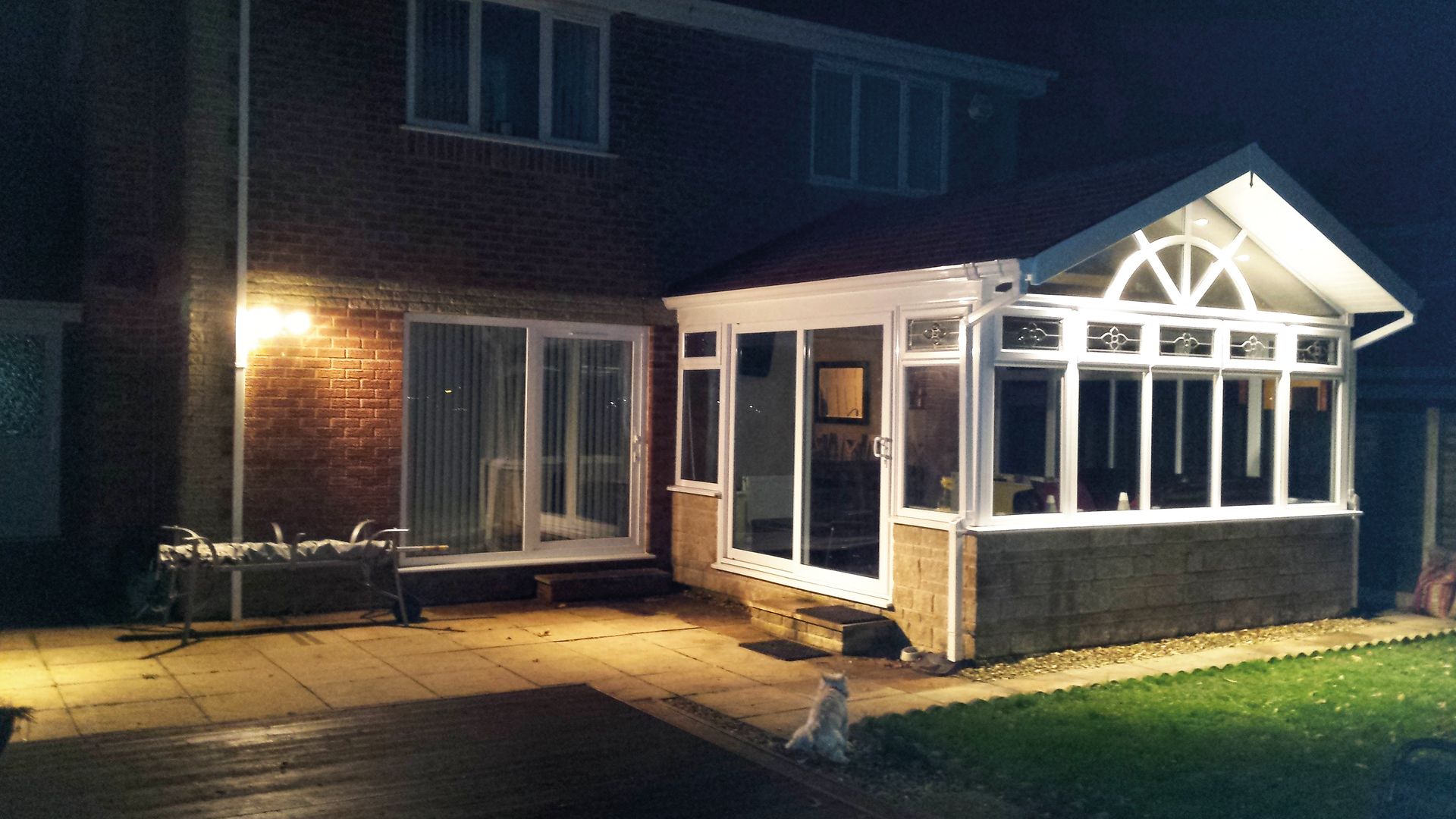 A brick house with a lit-up sunroom at night, patio in front.