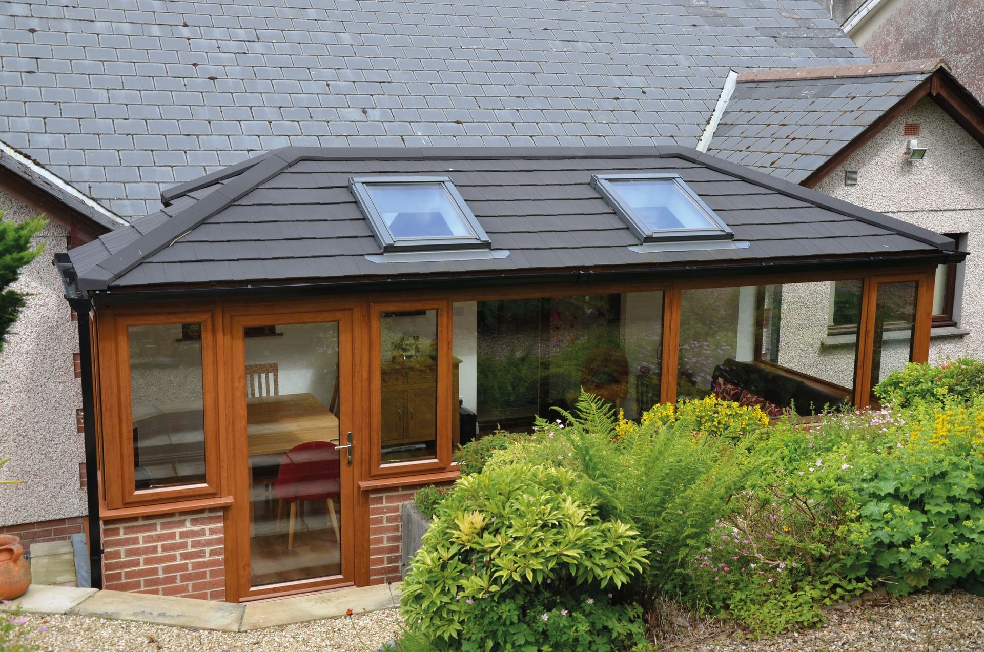 Sunroom addition with a brick base, glass walls, wood trim, and skylights, attached to a house.