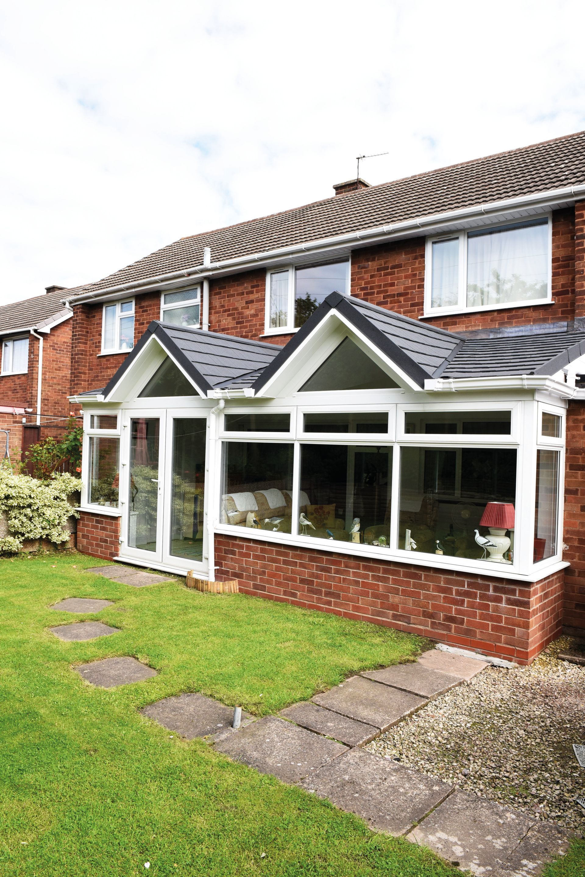 Brick home with glass-walled sunroom, slate roof. Stone path leads across the green lawn.
