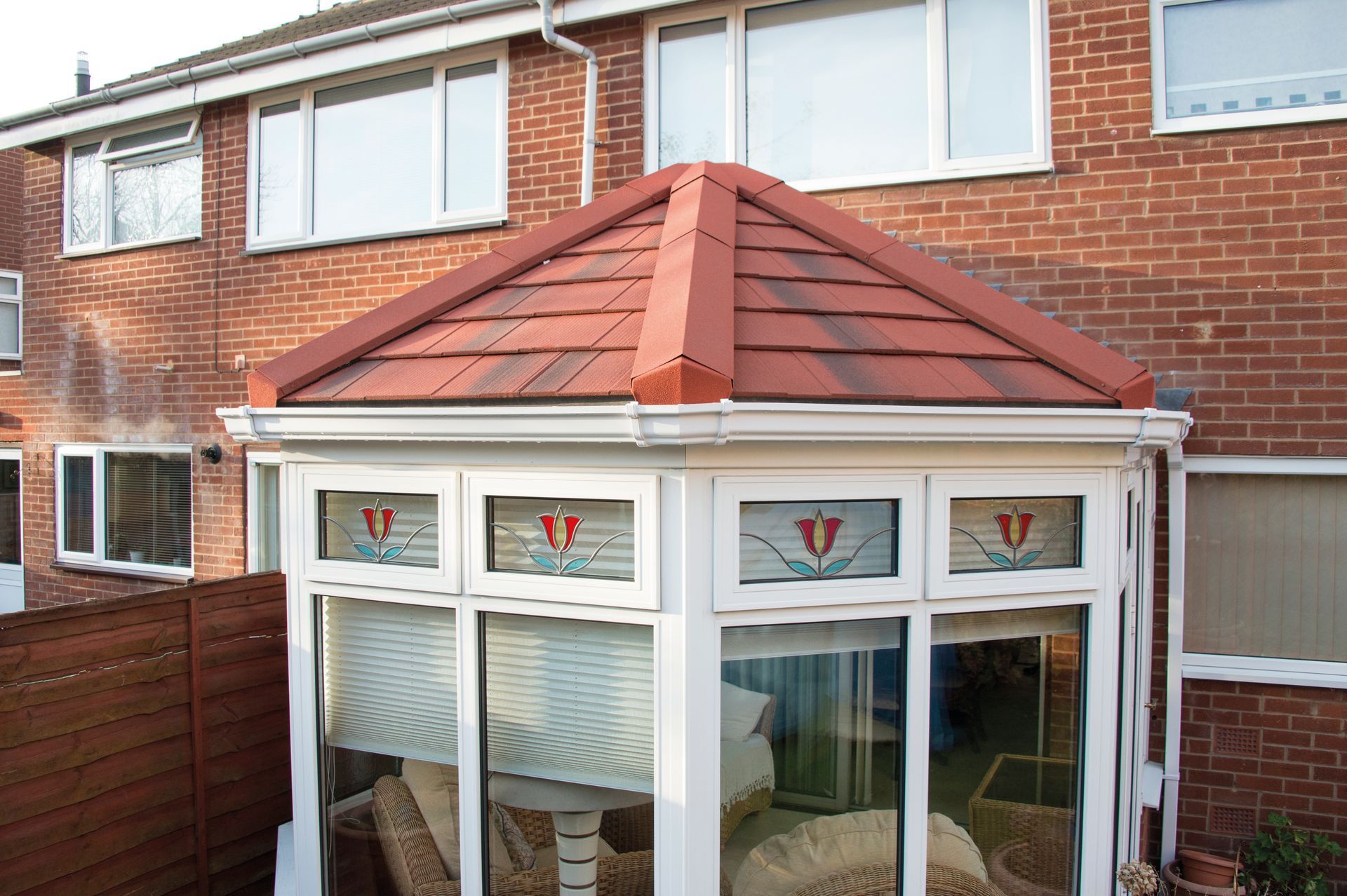 Conservatory with red tiled roof, white frame, stained glass windows, set against brick building.
