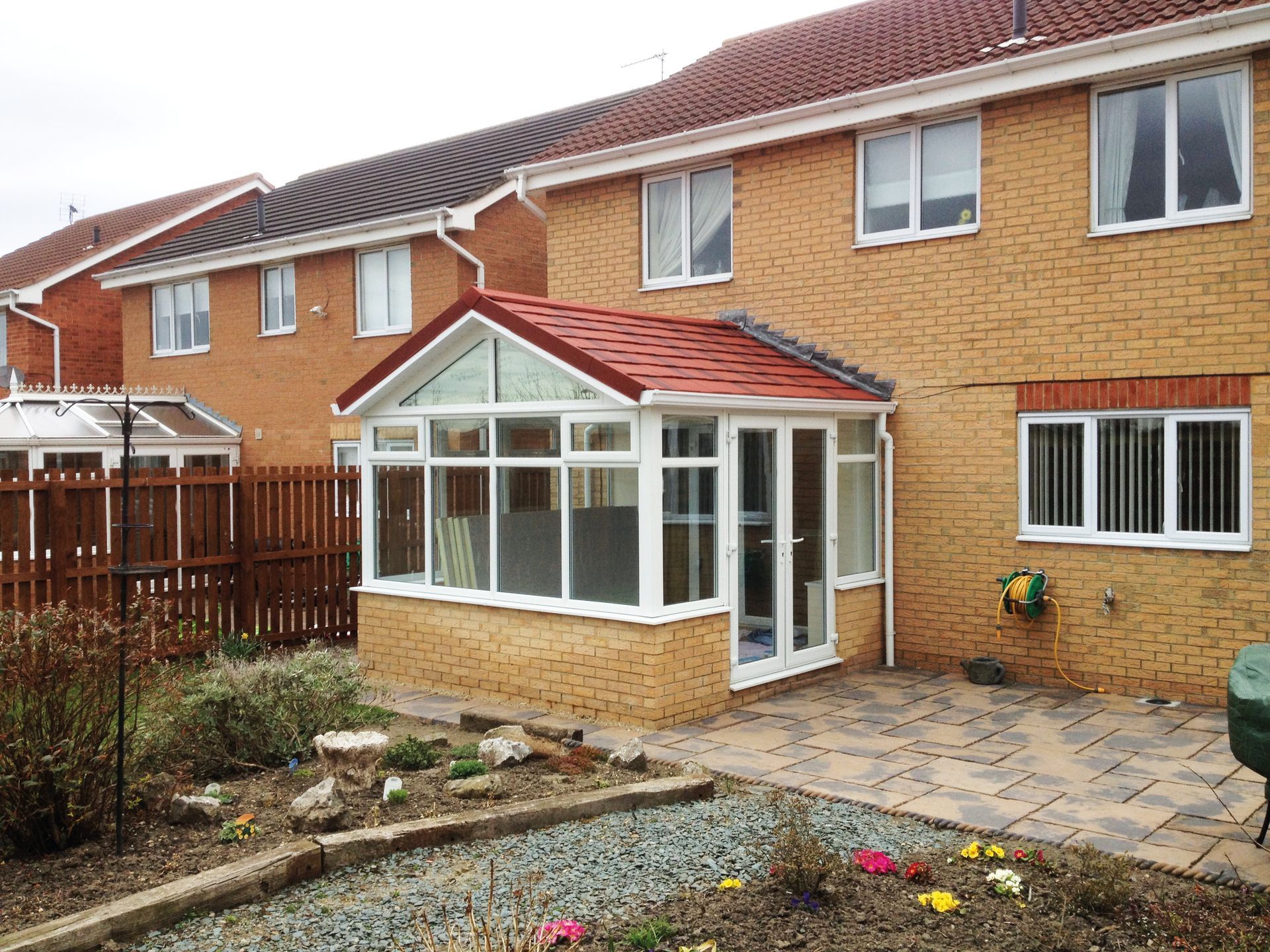 Sunroom addition to a brick house with a red tiled roof, surrounded by a garden with a brick patio.