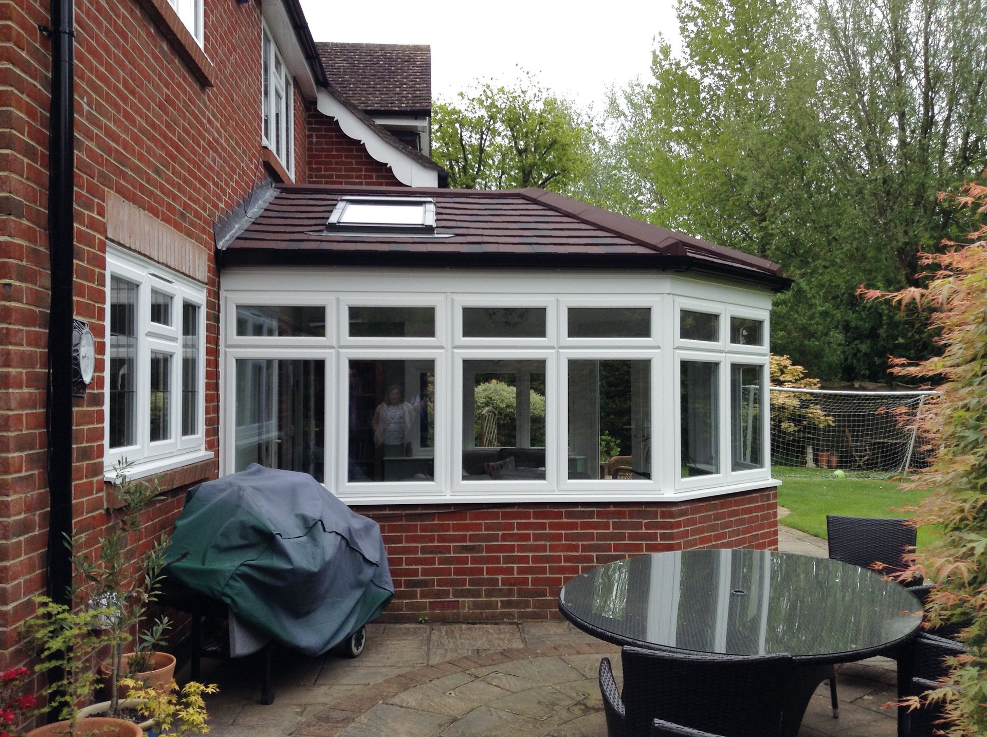A brick house with a white-framed conservatory, red roof, and a patio with outdoor furniture.