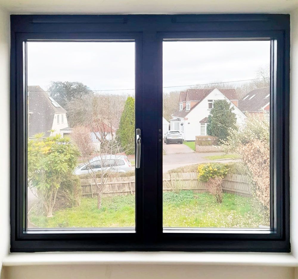 A black window with a view of houses, trees, and a car on a cloudy day.