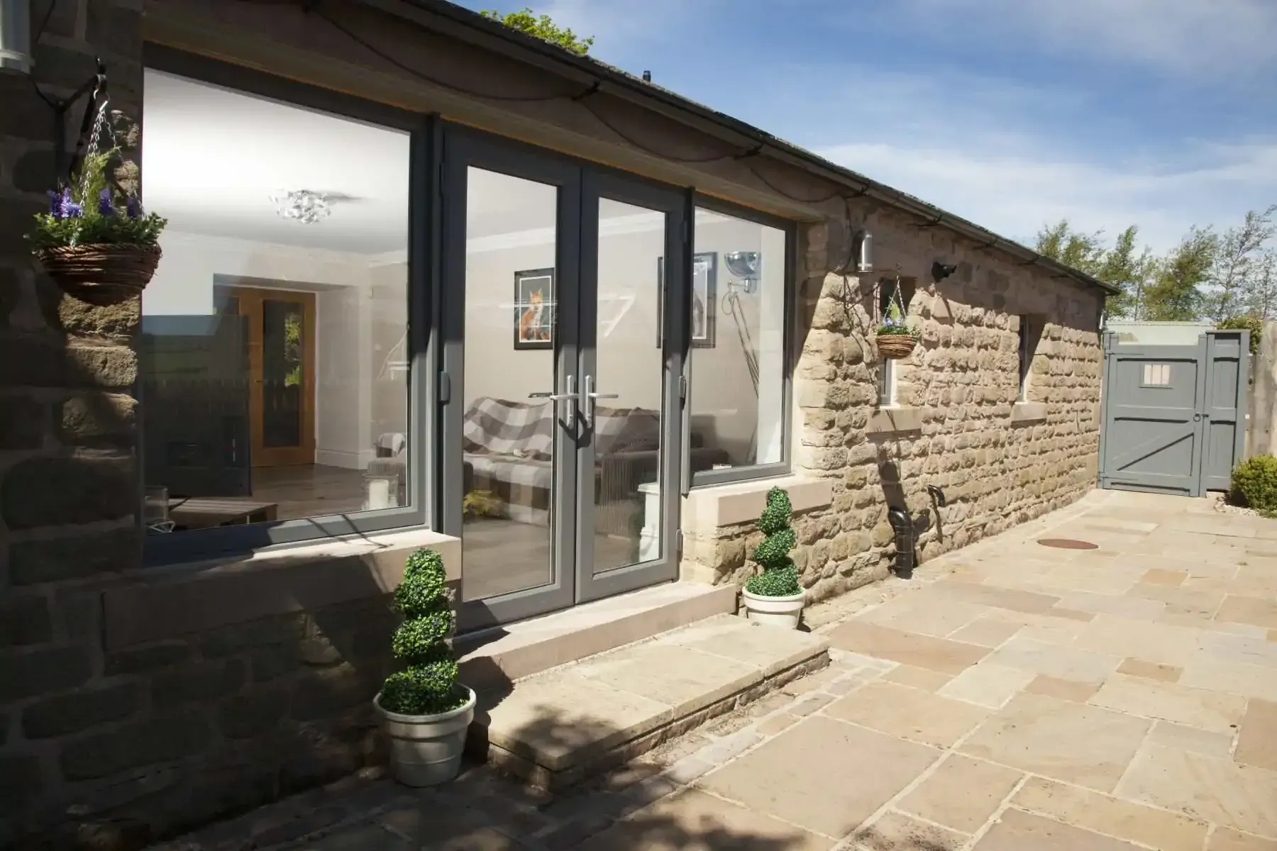 Exterior of stone building with glass doors, patio, potted plants, and gray trim.