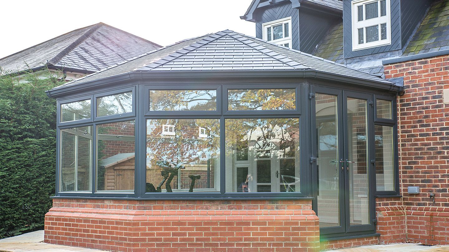 Octagonal conservatory attached to a red brick house, with dark grey framing and a glass roof.
