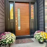 A wooden front door with sidelights, flanked by fall mums in pots.
