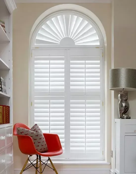 White shutters on arched window, red chair, and owl lamp.