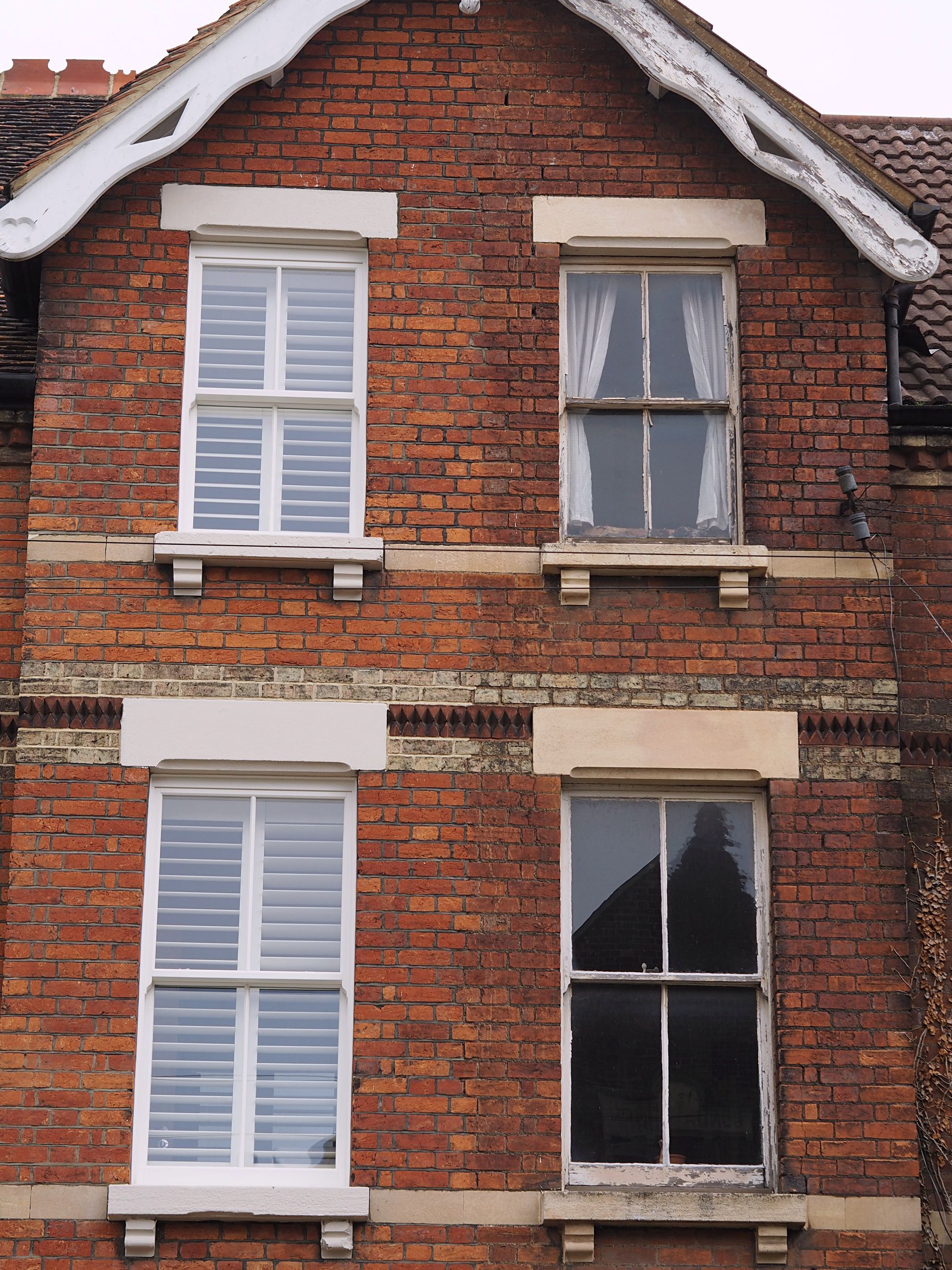 Two-story brick building with four white-framed windows. The top two windows have white drapes and shutters.