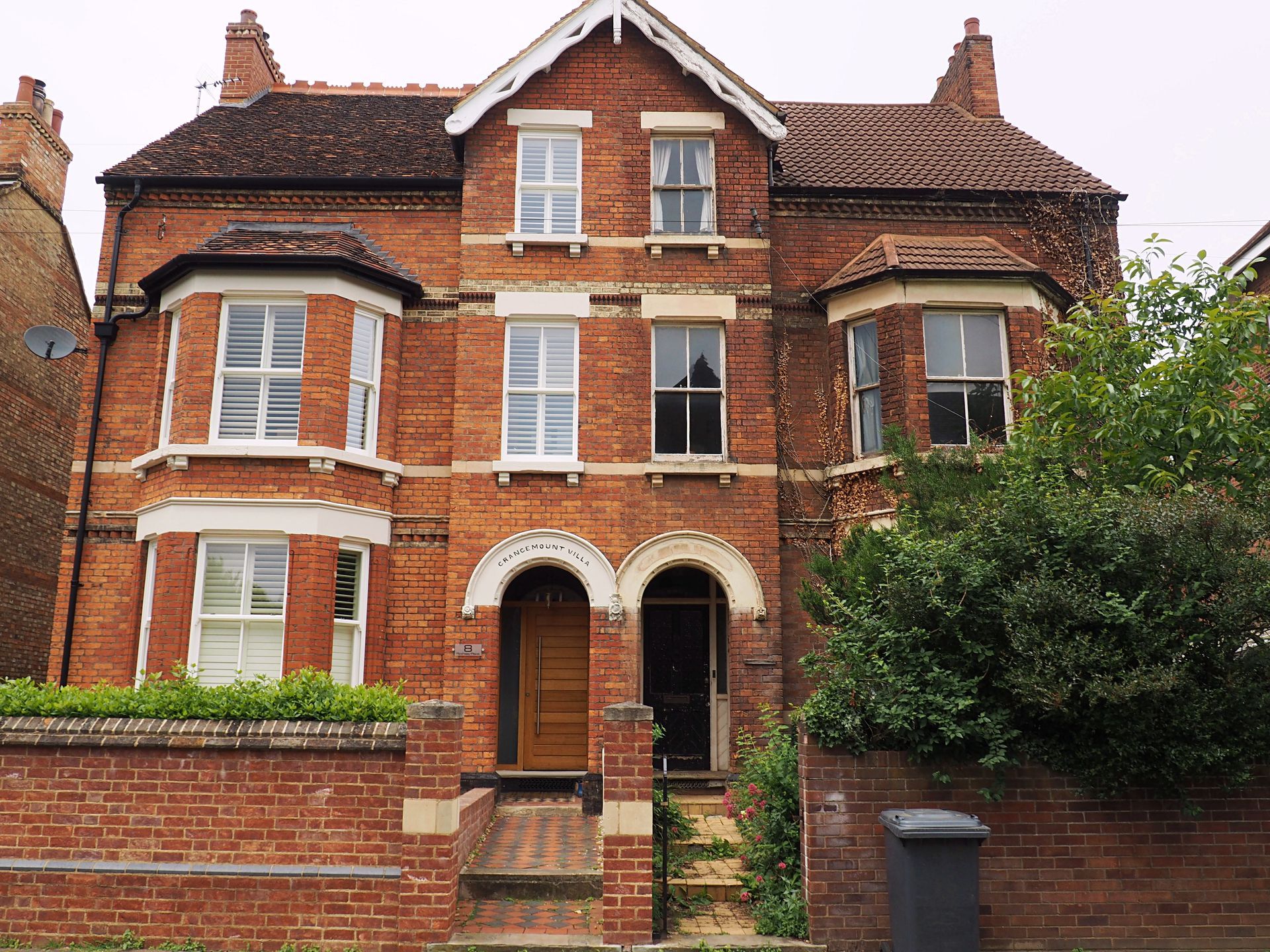 Brick two-story house with bay windows, arched doorways, and a small front garden.