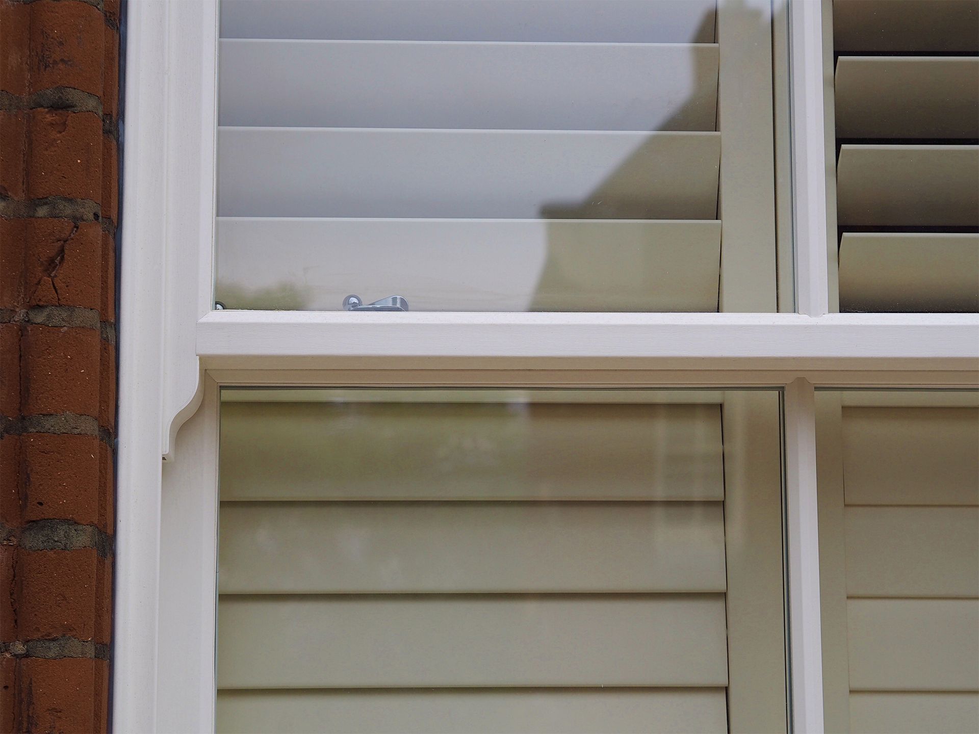 White louvered shutters in a window frame against a brick wall.