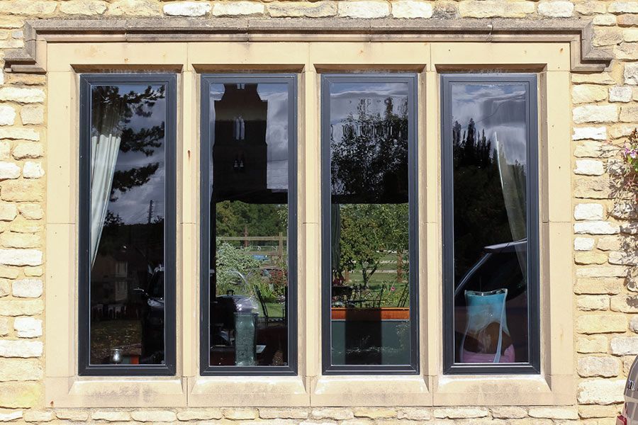 Four tall black-framed windows with reflections in a stone facade.