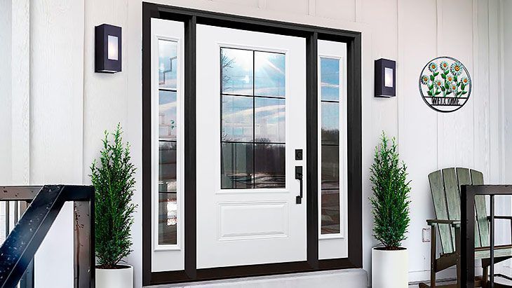 White front door with glass panels, flanked by green plants and black sconces on a white exterior.