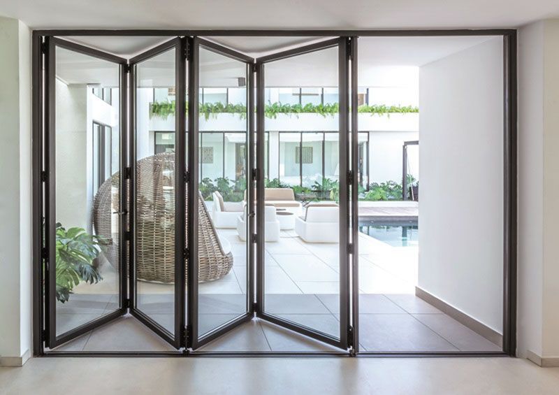 Folding glass doors open to a patio with white furniture and a pool.