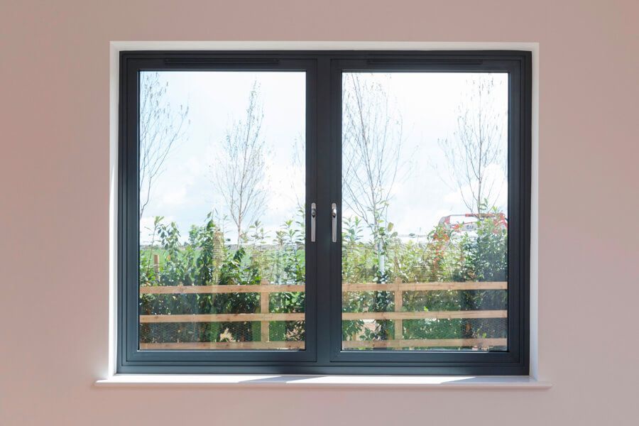 Dark-framed double window with view of trees and fence, set in a light pink wall.