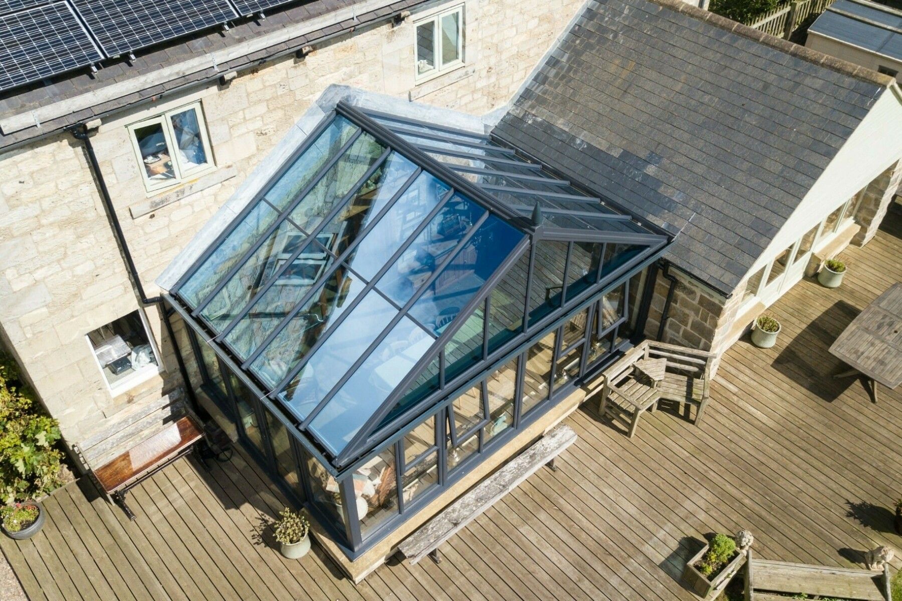 Glass-roofed conservatory attached to a stone building, with a wooden deck.