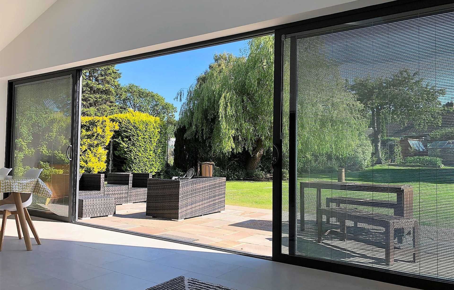 Open sliding doors reveal a backyard patio with seating, lush green trees, and a blue sky.