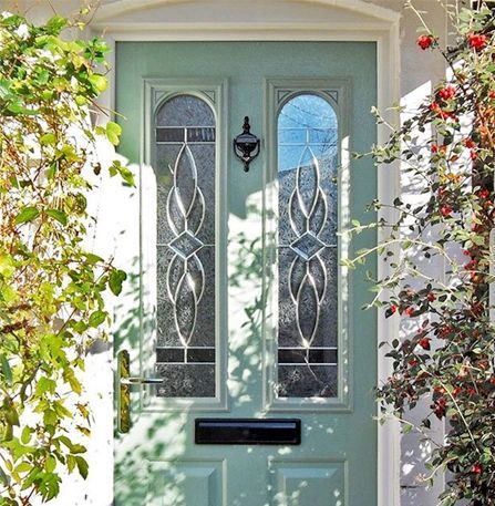 A light green front door with stained glass panels and a black knocker, partially framed by greenery.