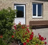 Brick building with red flowers, a white door, window, and a bench.