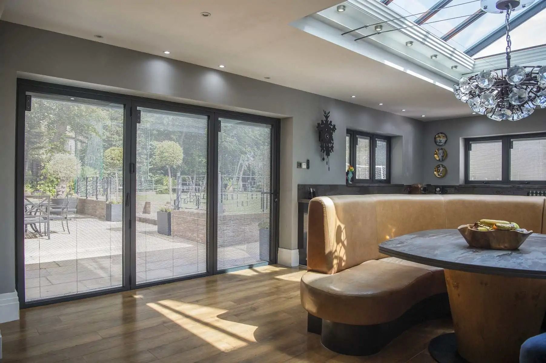Interior of a modern dining space with large glass doors, tan seating, and a skylight.