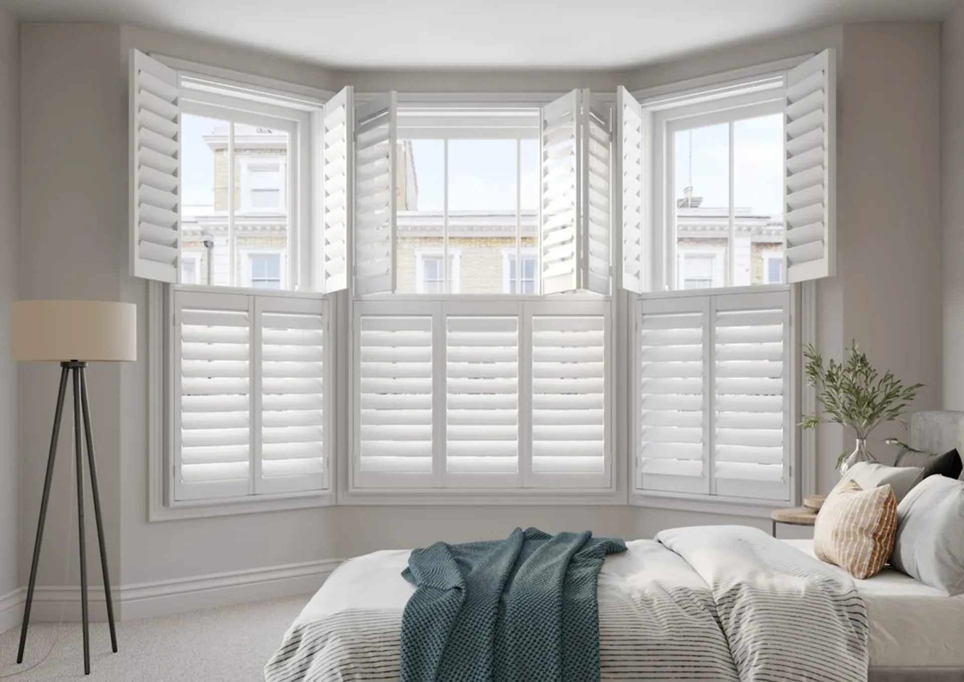 White shuttered windows in a bedroom, centered over a bed with a blue blanket.