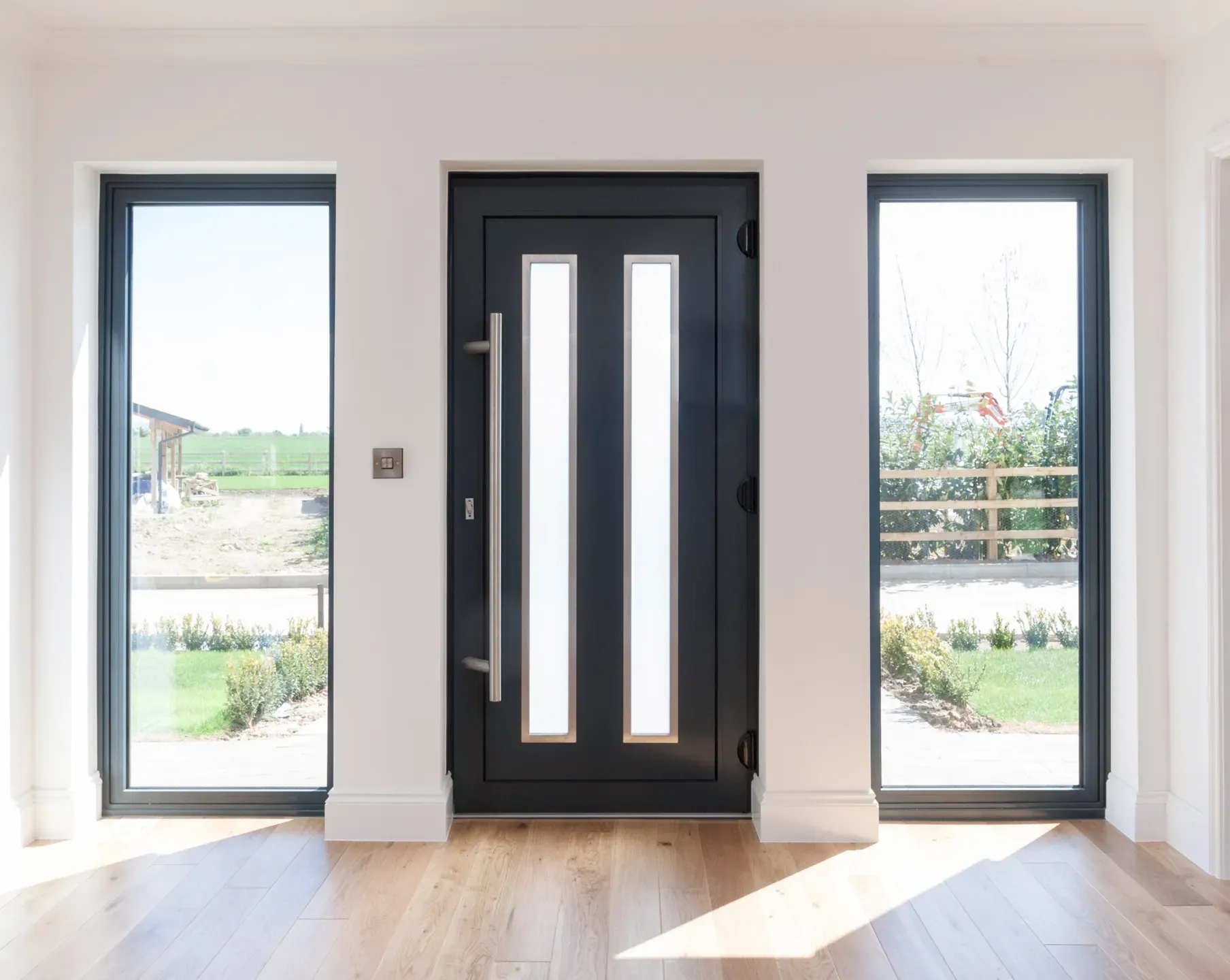 Black door with vertical glass panels, flanked by tall windows, wooden floor.