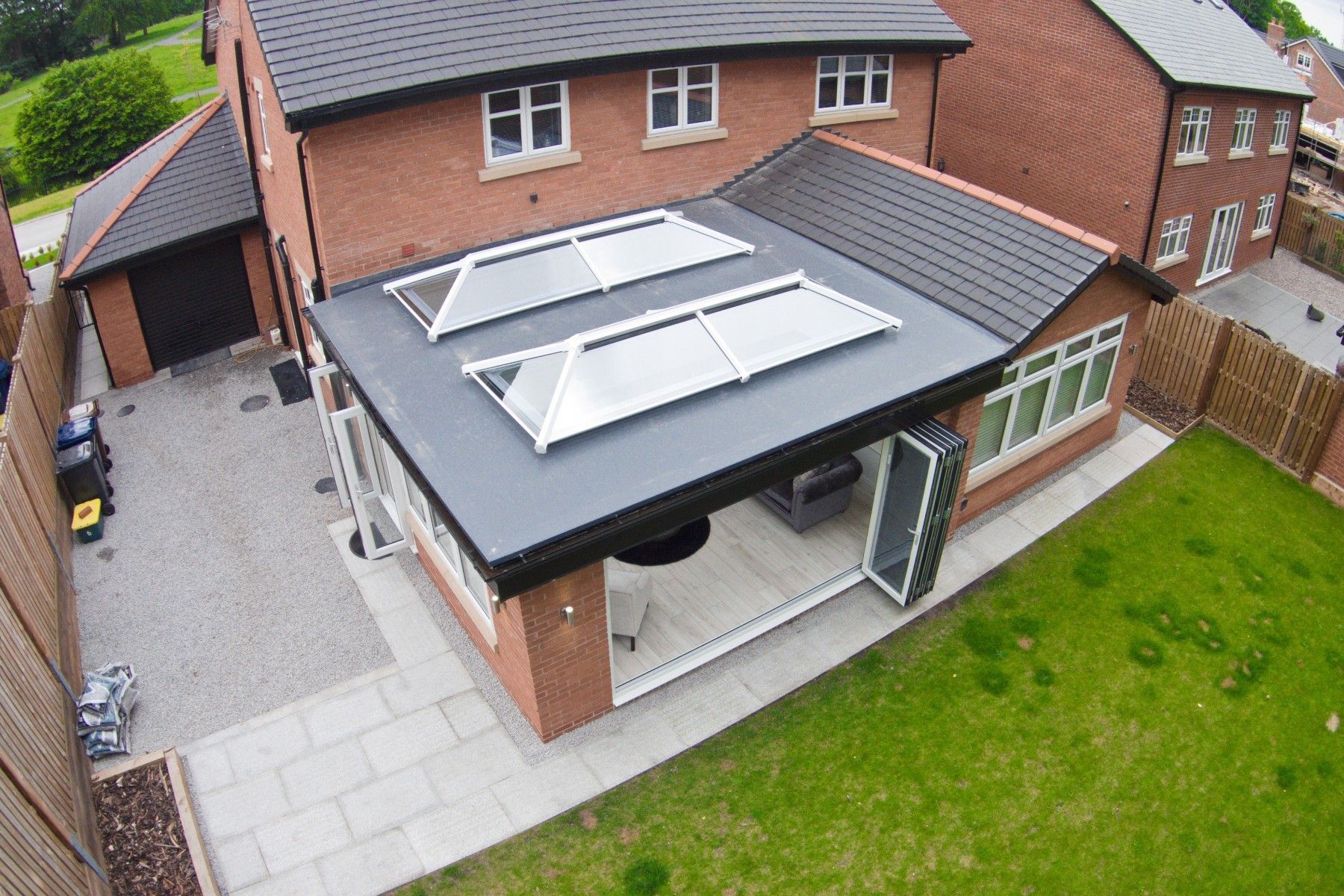 A brick house extension with a flat roof, two skylights, and open sliding doors, adjacent to a lawn and a driveway.