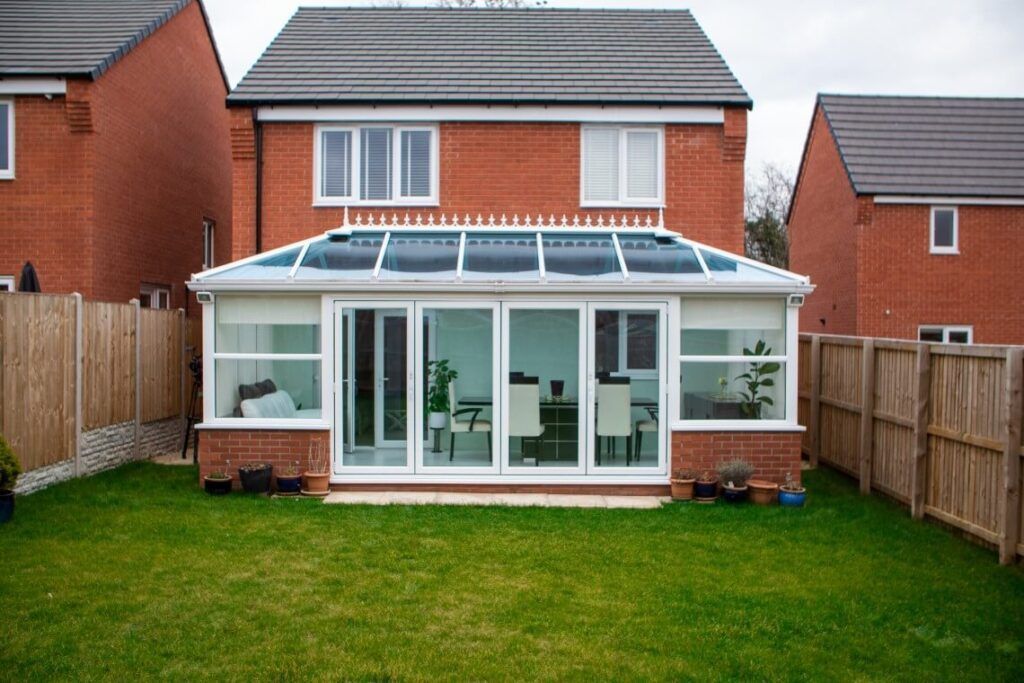 Sunroom addition to a brick house, with glass doors, white trim, and a tiled roof. Green lawn.
