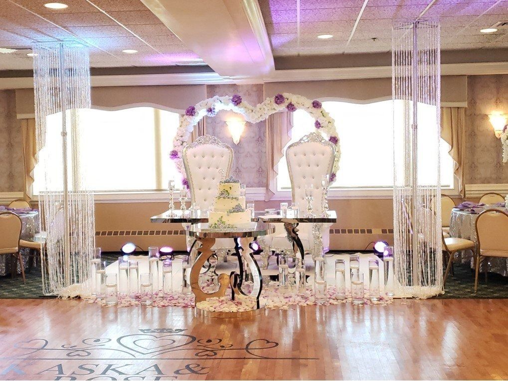 Decorated wedding reception stage with white chairs, floral arch, and lights on a polished wooden floor
