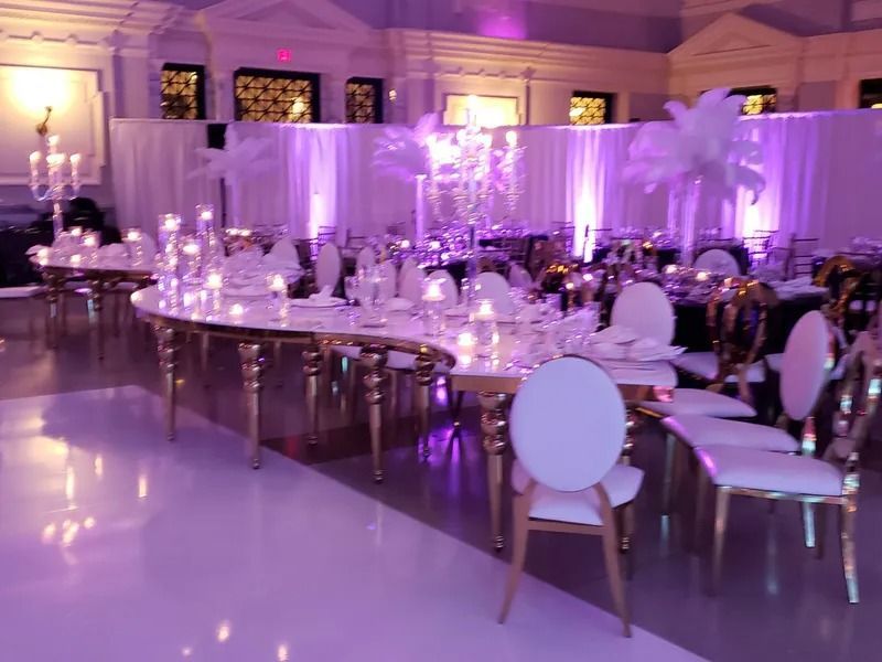 Elegant banquet hall with long decorated tables, white chairs, and purple lighting