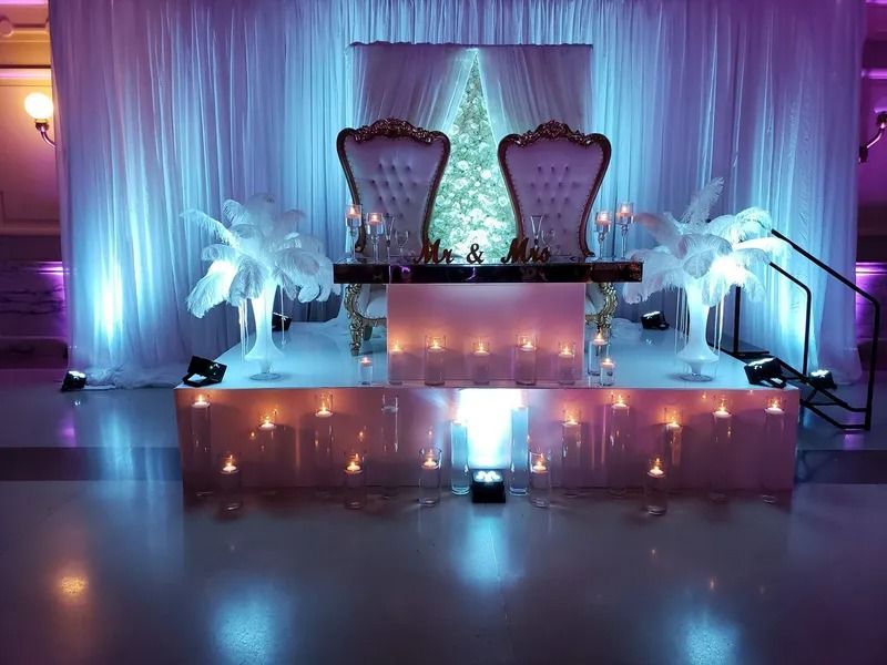 Elegant lit stage with two ornate chairs, white drapes, and blue-purple accent lighting