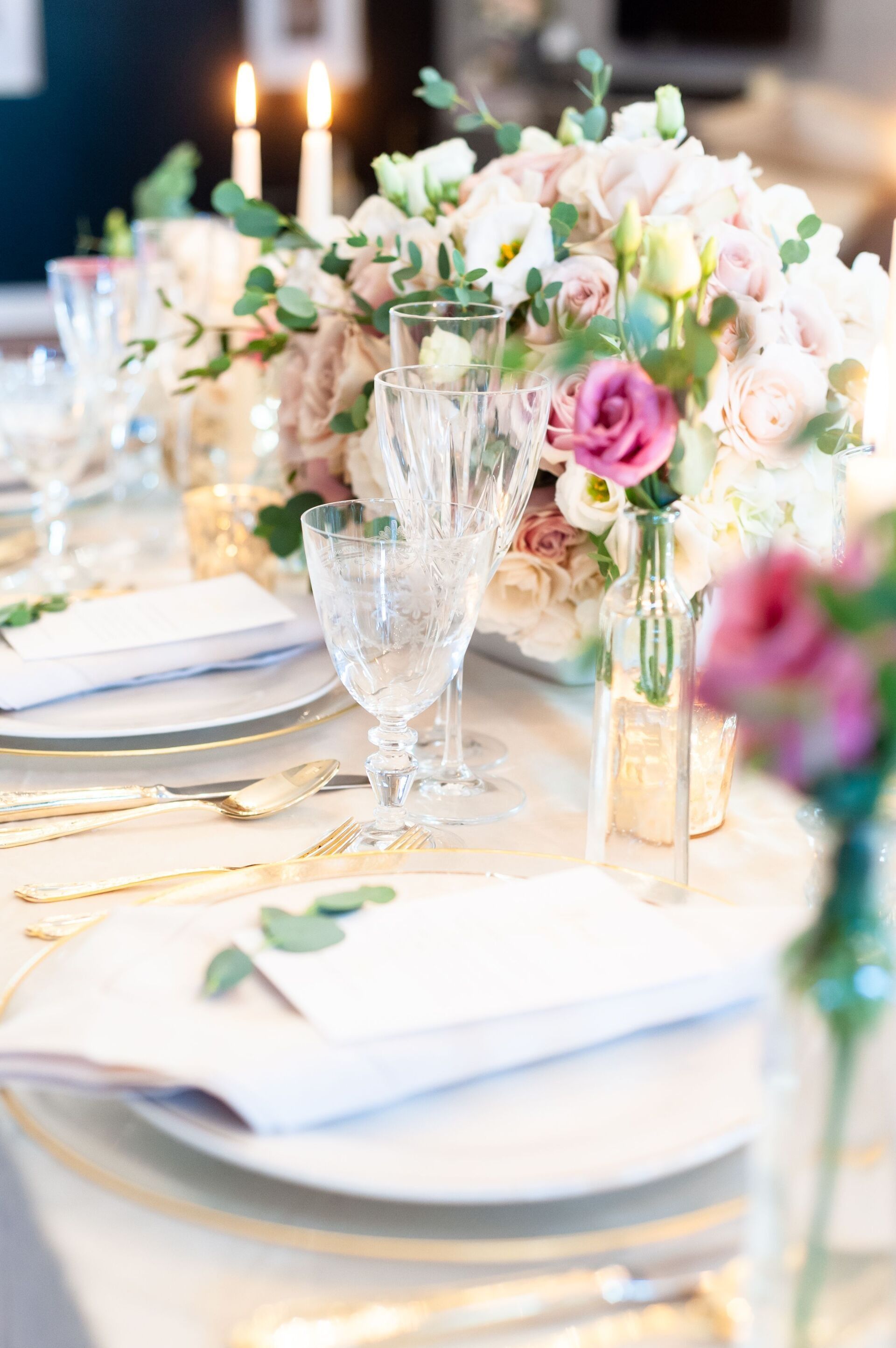 Elegant banquet table with white plates, gold accents, crystal glassware, and pastel floral centerpiece