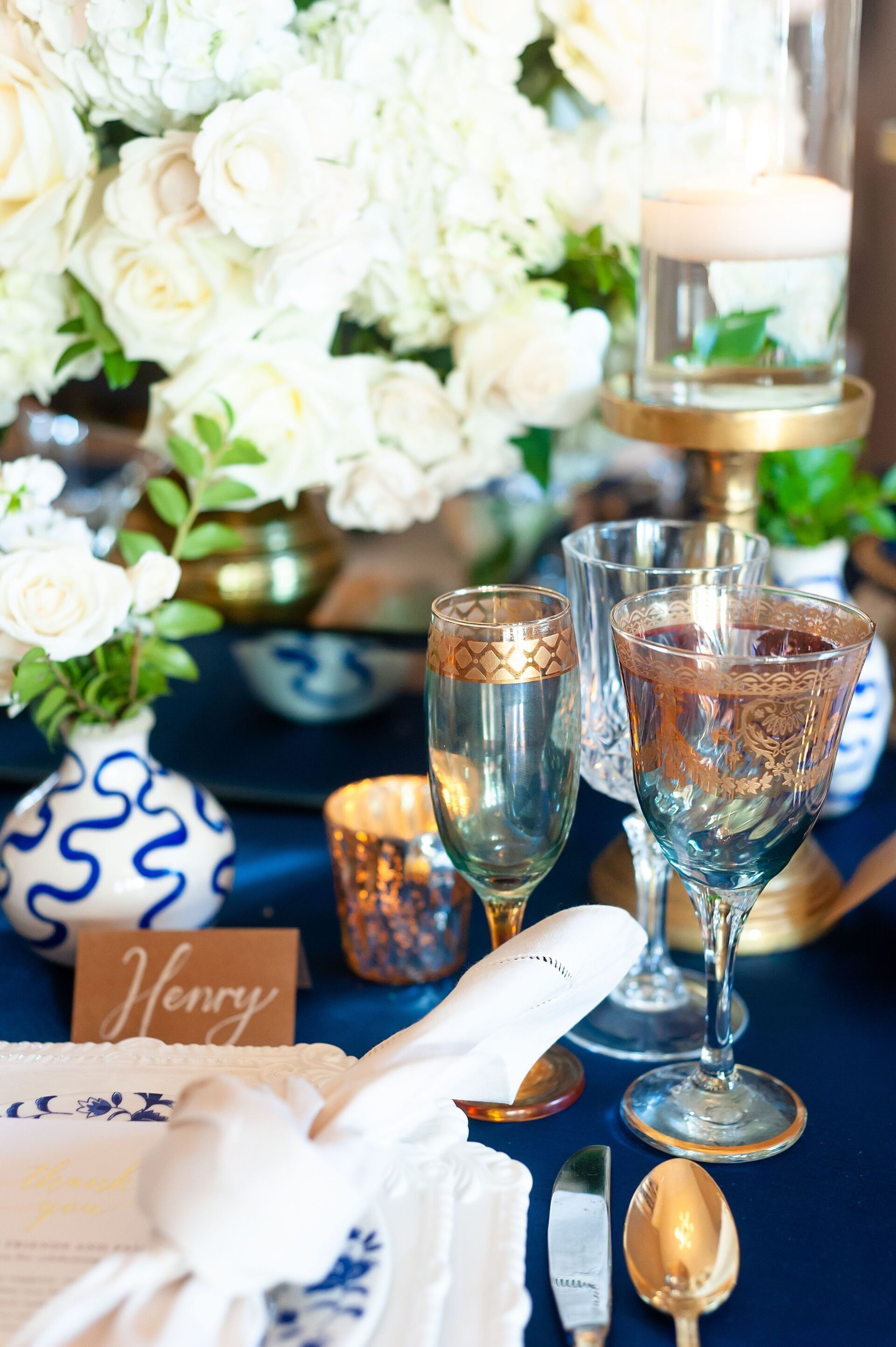 Elegant table setting with white flowers, blue-and-white decor, candles, and crystal goblets