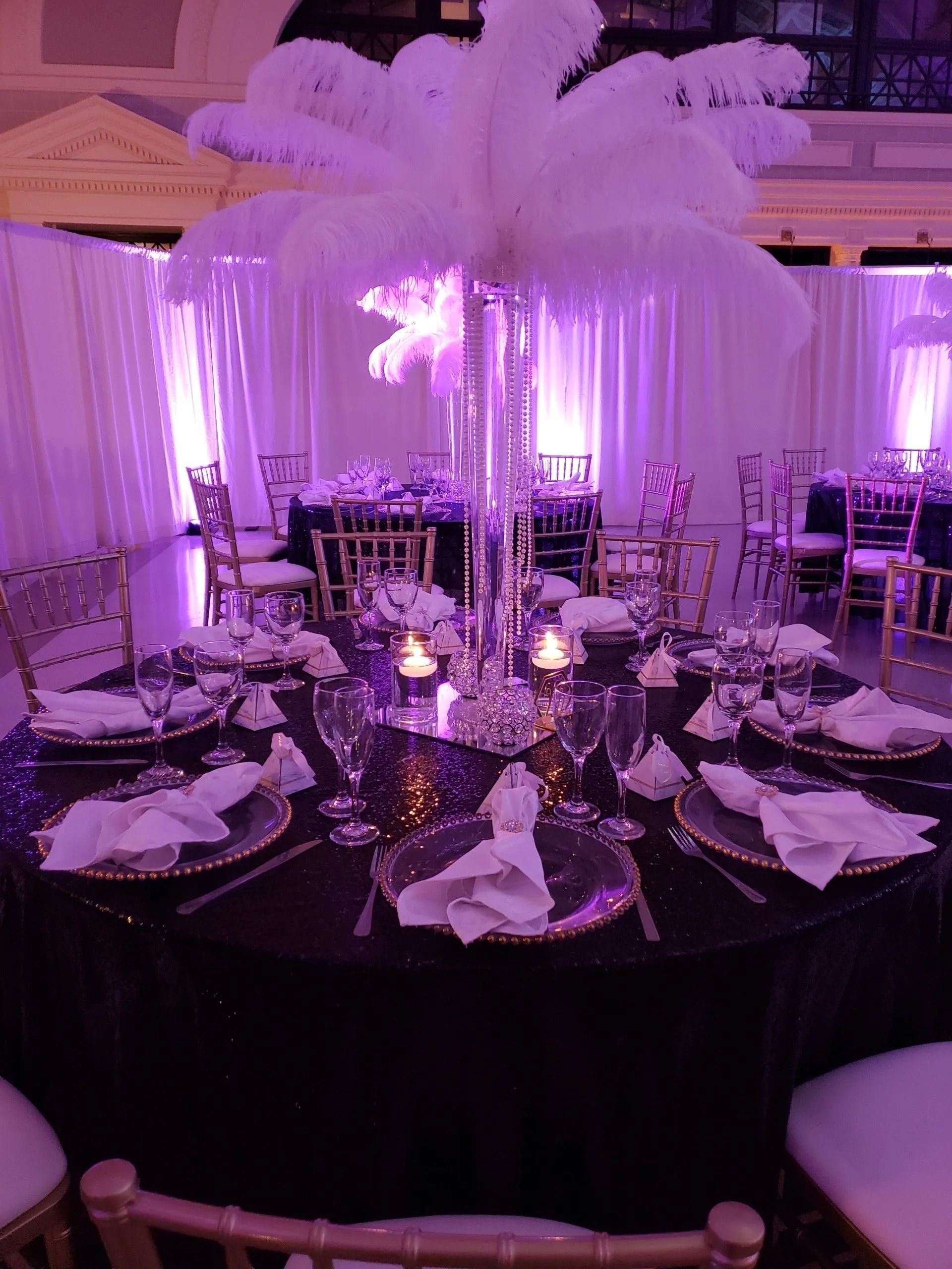 Purple-lit banquet table with feather centerpiece, surrounded by set chairs and elegant table settings