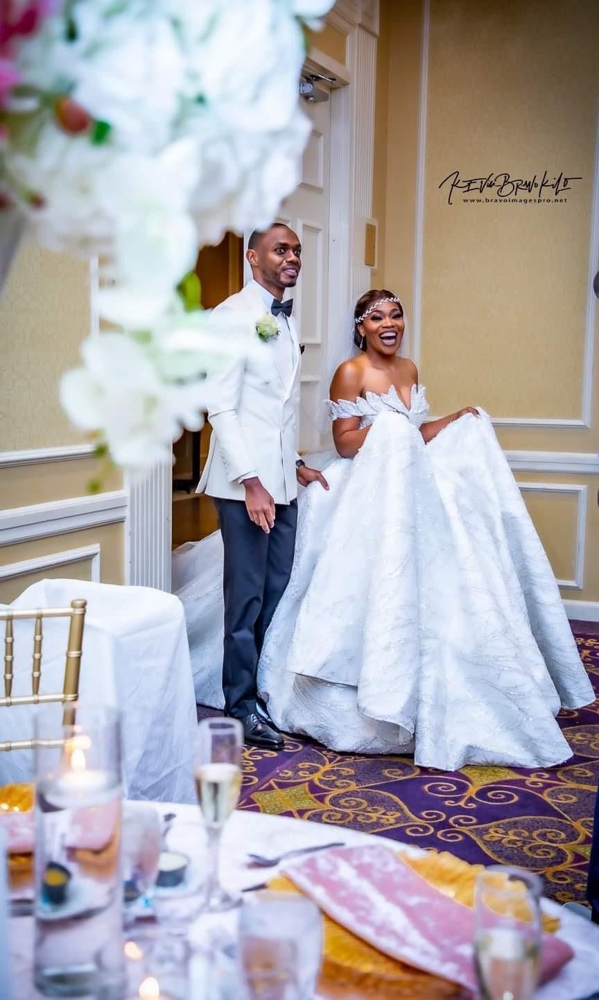 Bride and groom smiling in white wedding attire in a decorated banquet hall