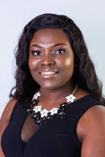 Portrait of a smiling woman in a black dress and floral necklace against a light gray background
