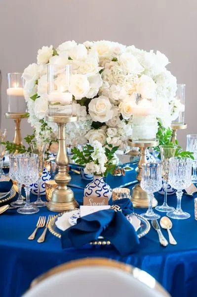 Blue-draped banquet table with white floral centerpiece, gold candlesticks, and place settings
