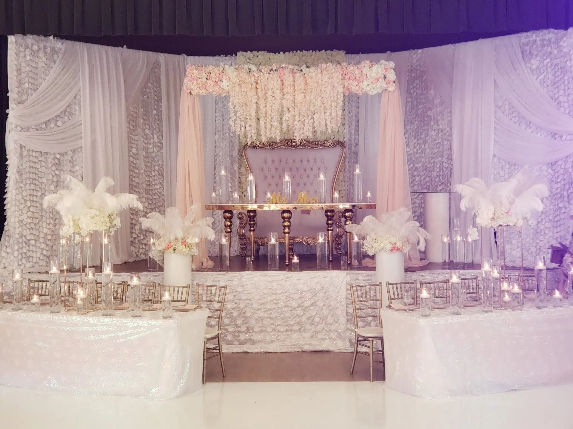 Lavender and white wedding stage with floral decor, draped backdrop, and mirrored tablescapes
