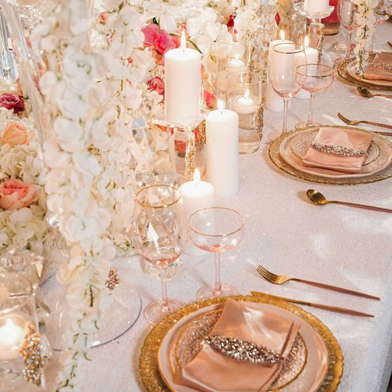 Elegant pink-and-gold table setting with candles, flowers, glassware, and plated napkins
