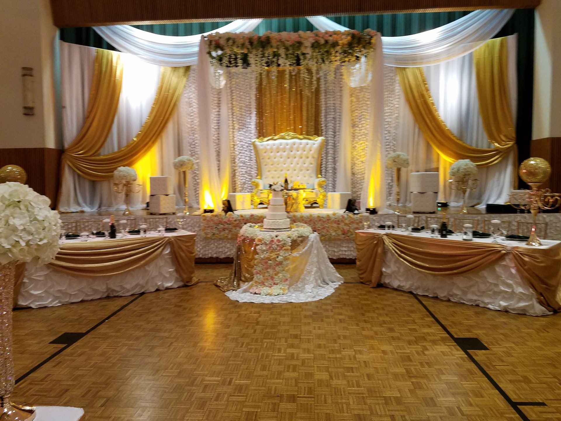 Elegant banquet hall with gold drapes, white floral decor, and set dining tables for a formal event