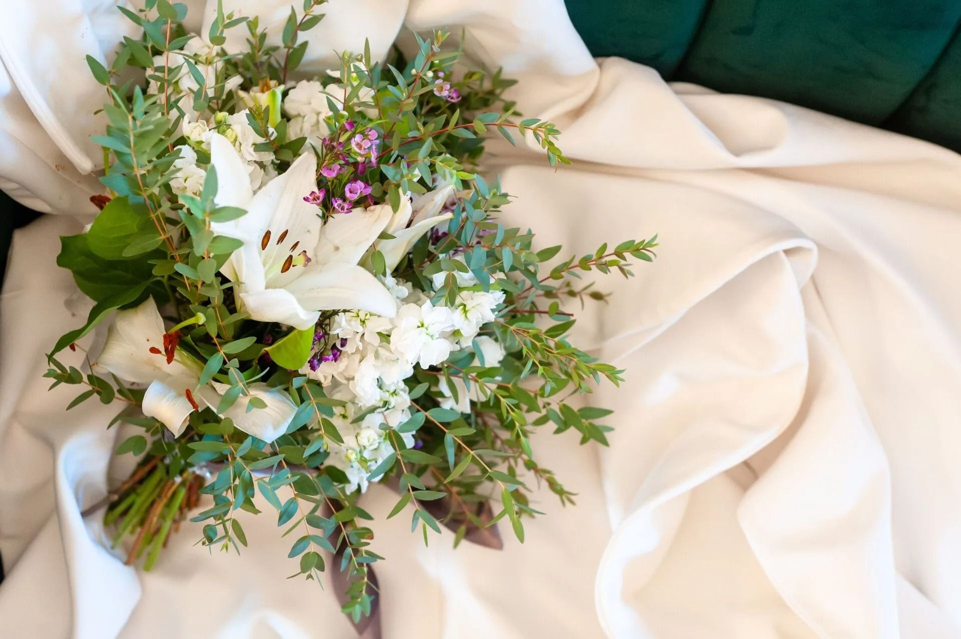 White floral bouquet with greenery on cream fabric, with a teal cushion in the background