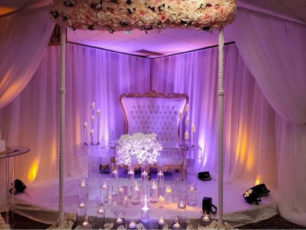 Lavender-lit wedding stage with draped canopy, ornate chair, flowers, and candles