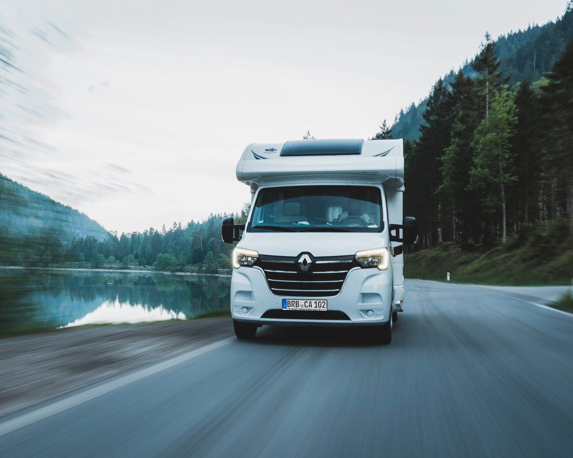 Wohnmobil auf einer Straße durch eine bewaldete Berglandschaft