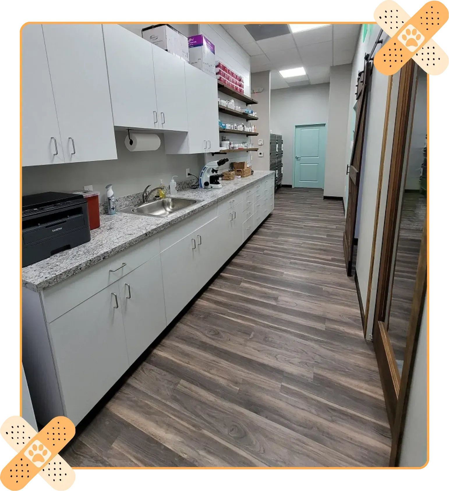 Narrow clinic hallway with white cabinets, granite counters, wood-look floor, and teal door at the end