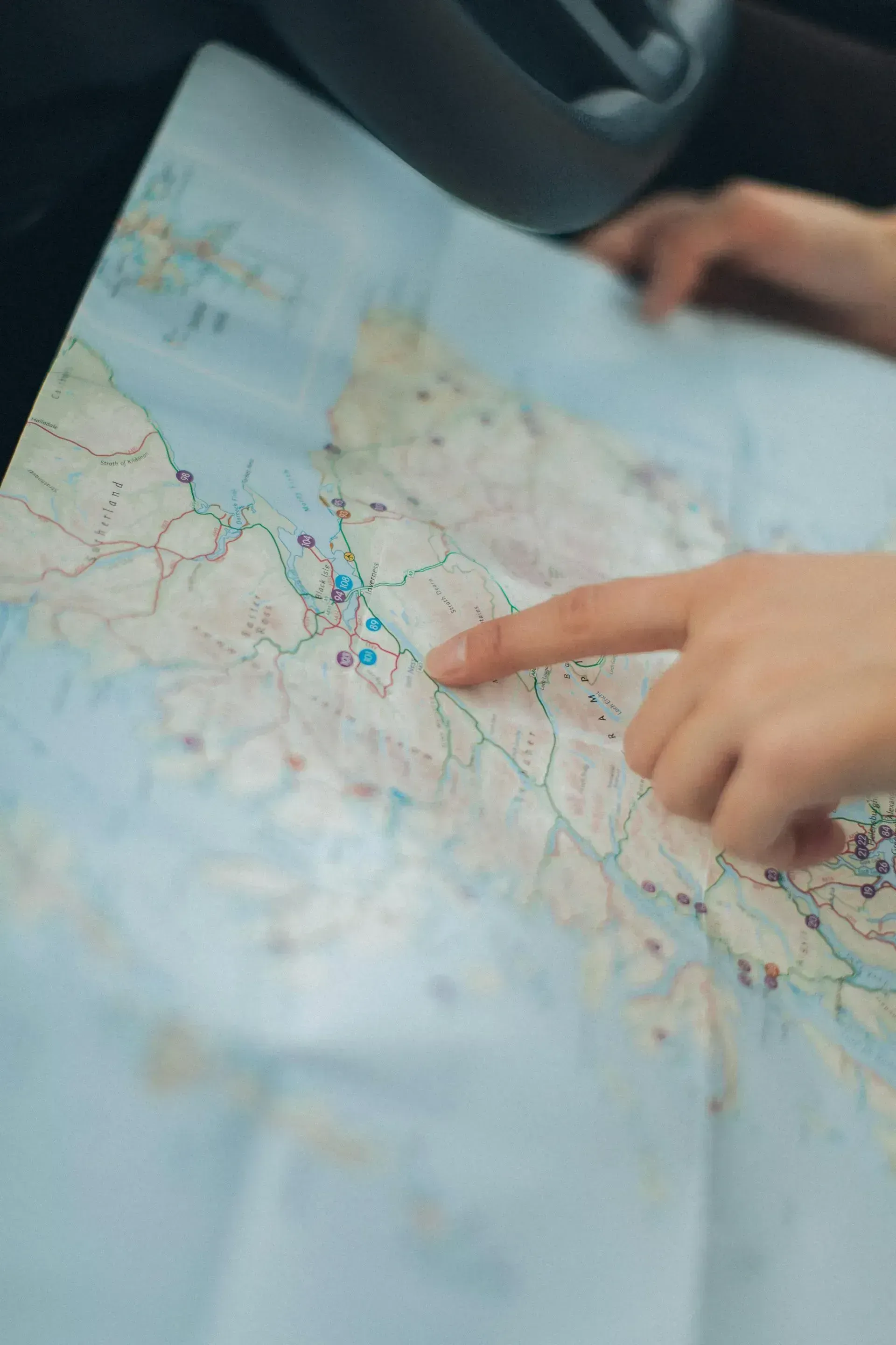 Hand pointing to a road map spread across a car seat