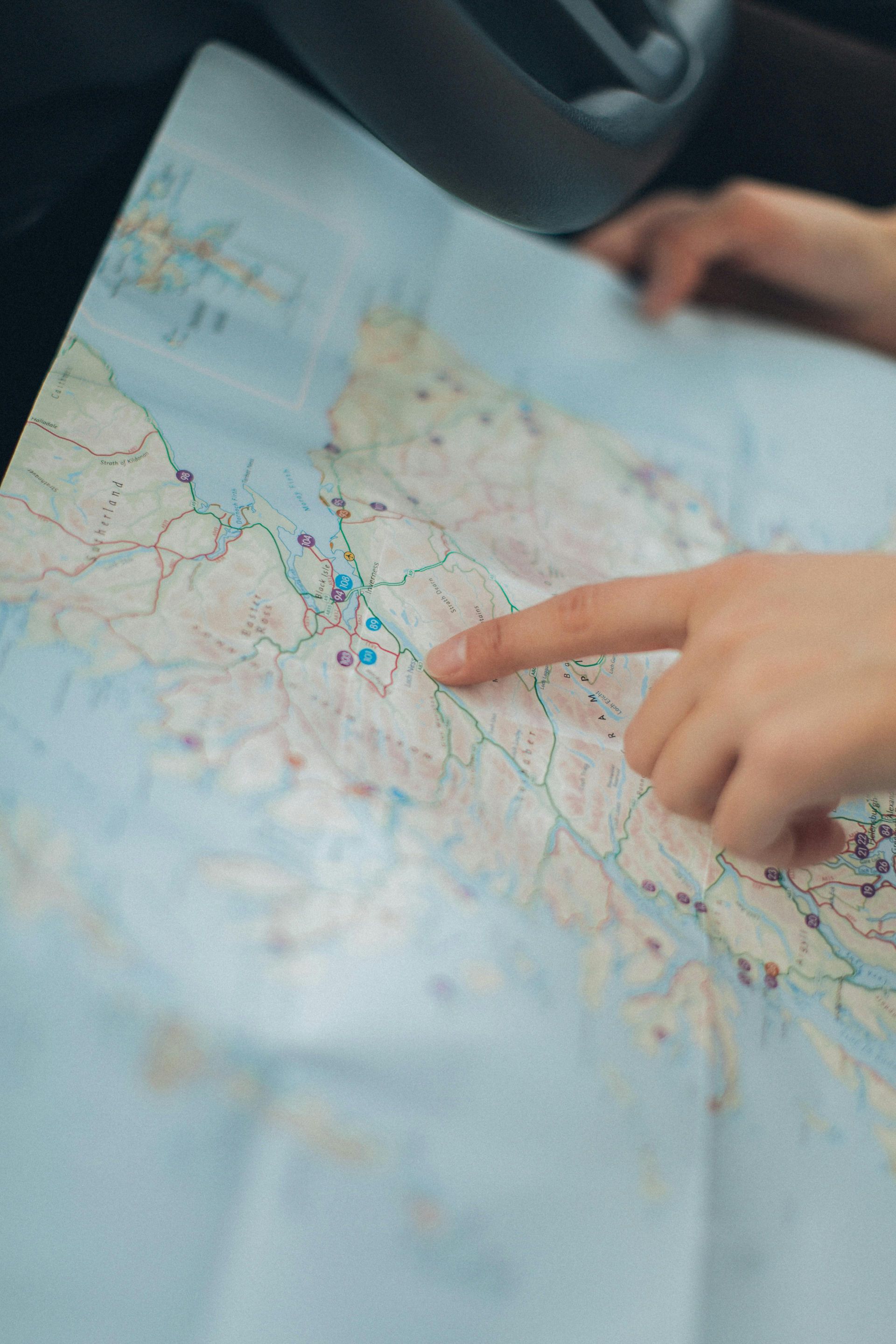 Hand pointing to a road map spread across a car seat