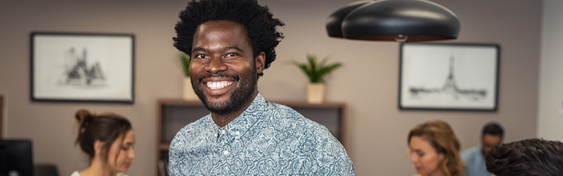 A man is smiling in front of a group of people in an office.
