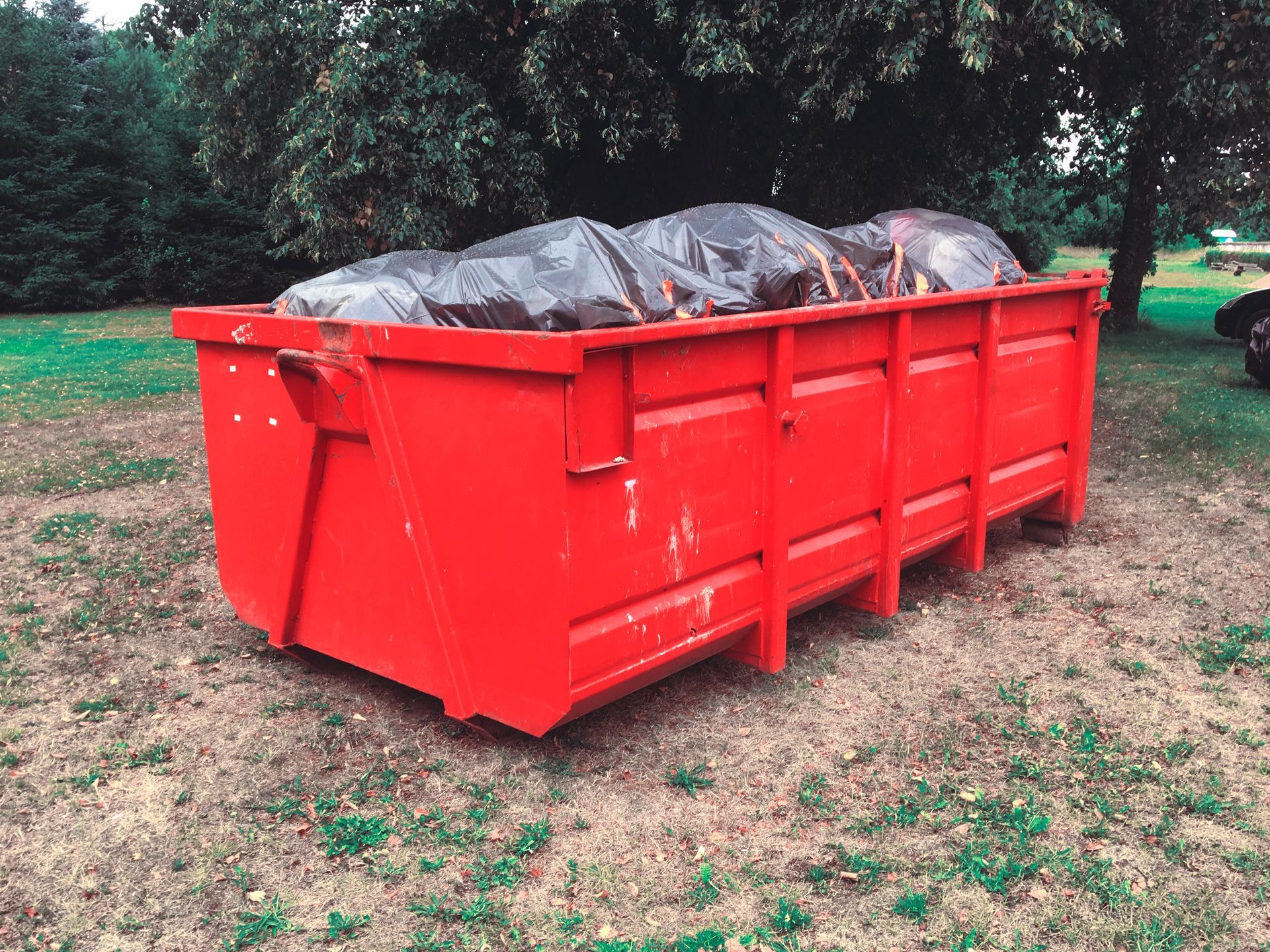 A large red dumpster filled with trash is sitting in the grass.